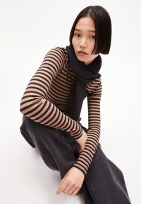 Langärmliges Oberteil mit horizontalen braunen und marineblauen Streifen, kombiniert mit einem strukturierten dunklen Schal und lässigen dunklen Hosen. Glatte Stoffoberfläche.