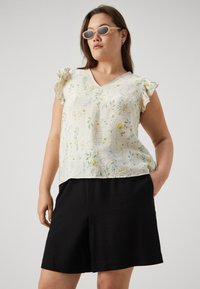Haut à imprimé floral en crème avec des manches bouffantes, décolleté en V, tissu texturé ; associé à un short noir ample.