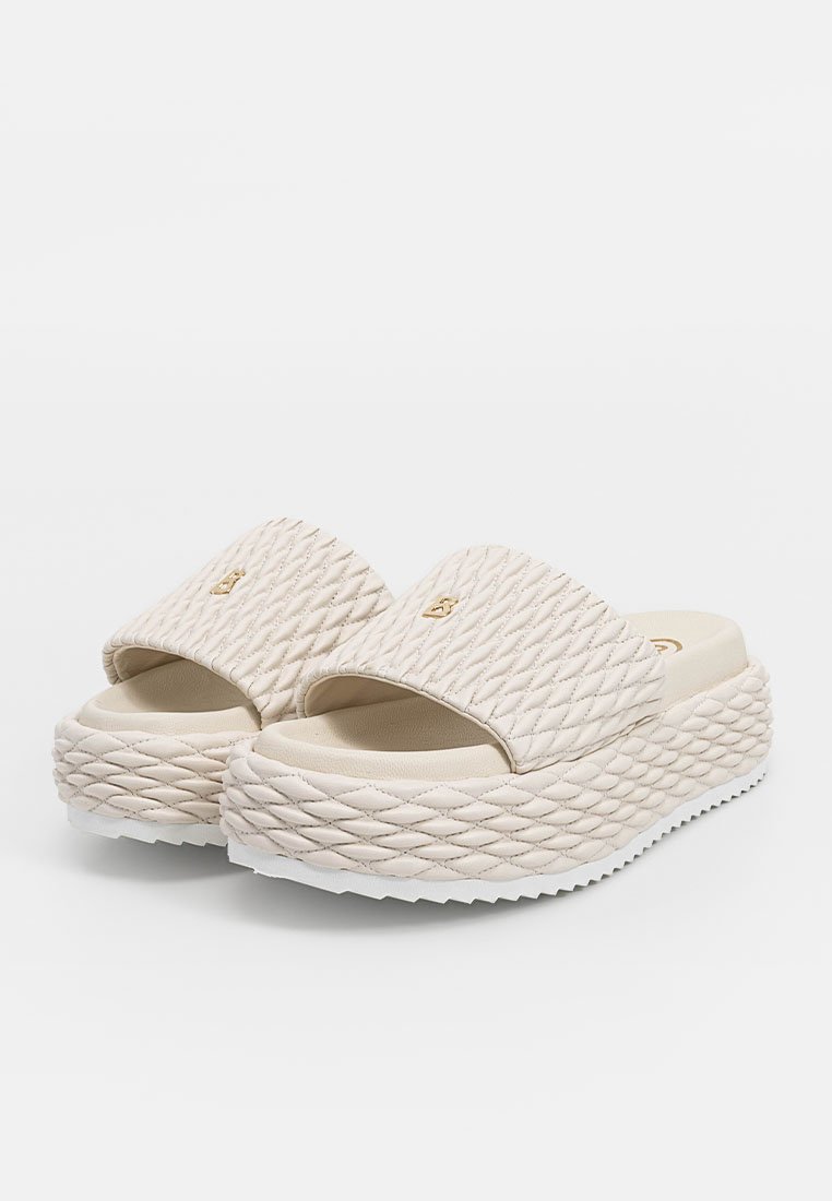 Beżowe sandały na platformie z przeszywanym wzorem na górnym pasku i grubą plecioną podeszwą. Wyposażone w złoty akcent z logo.