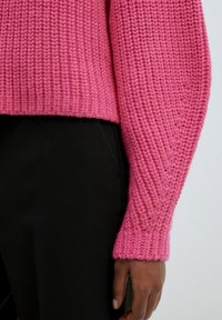 Pull en laine rose avec un motif texturé, doté d'un ourlet et de bords-côtes. Le tissu semble doux et épais, ce qui renforce le design global.