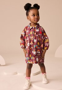 Vestito viola con motivi di animali e cibo, chiusura con bottoni sul davanti, vita arricciata, maniche lunghe e due tasche; abbinato a scarpe da ginnastica bianche e calzini rosa.