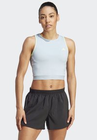 Lyseblå ærmeløs crop top med gule detaljer og et tekstureret taljebånd, parret med sorte shorts med elastisk talje.
