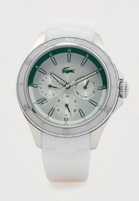 Montre avec cadran argent et vert, trois sous-cadrans et bracelet en silicone blanc, affichant 11:10:38, avec le logo crocodile de Lacoste.