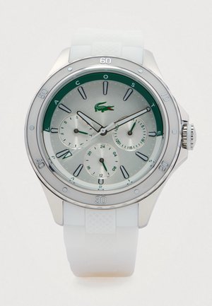 Montre avec cadran argent et vert, trois sous-cadrans et bracelet en silicone blanc, affichant 11:10:38, avec le logo crocodile de Lacoste.
