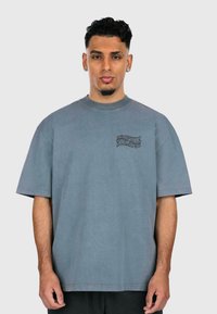 Gray oversized t-shirt made of soft cotton, featuring short sleeves and a round neck. Notable front design with black lettering on the left chest.