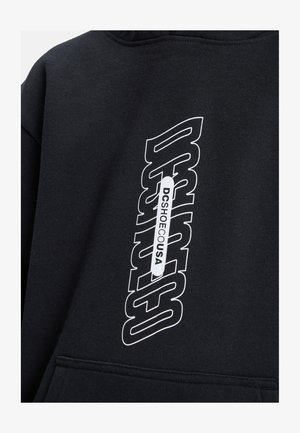 Sweat à capuche noir présentant un grand graphisme textuel blanc avec "DCSHOE" et "DCSHOEUSA". Le matériau semble doux avec une texture lisse.
