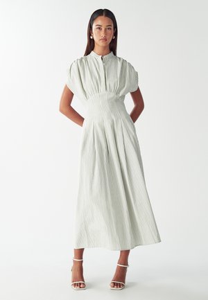 Light green striped maxi dress with short puff sleeves and a high neckline. Flowing texture with defined waistline. Paired with white sandals.