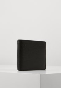 Billetera de cuero negro con una superficie texturizada, forma cuadrada y un detalle de costura sutil. Cuenta con un diseño de doblez para un cierre seguro.