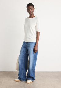 Pull court en tricot gris clair à manches courtes, jeans en denim bleu à jambe large et baskets beiges. Design simple avec une coupe décontractée et une texture douce.