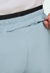 Los pantalones cortos deportivos de color azul claro cuentan con una cinturilla elástica con una banda negra y un bolsillo con cremallera en el costado para un almacenamiento seguro.