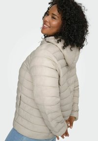 Bēšas krāsas pūkains virsjaka ar kapuci, izšūtu dizainu un sānu rāvējslēdzēja kabatām. Mīksta tekstūra ar horizontālu ribojumu visā virsmā.