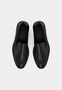 Sorte slip-on sko med en glat læderoverdel og en afrundet tå, der har et minimalistisk design uden synligt hardware eller dekorationer.