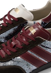 Gros plan sur des baskets bordeaux avec des sequins argentés métalliques, du daim marron foncé, des lacets bordeaux et la marque dorée "CAVAL" sur la languette.