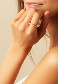 Guldring med en oval, tekstureret top, båret på en hånd med en naturlig hudtone. Baggrunden er neutral og blødt oplyst.