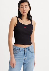 Must mustriba crop-top, millel laiad rihmad ja väike punane Levi's logo ees, kombineeritud helesiniste kõrge vöökohtadega teksadega.
