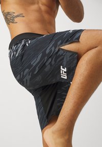 Black and gray patterned athletic shorts with a mesh panel, featuring a UFC logo on the lower leg and a slit for increased mobility.