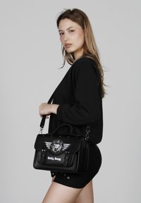 Bolso de mano negro con un asa superior y correa desmontable, adornado con un gráfico de Betty Boop, alas decorativas y tachuelas plateadas.