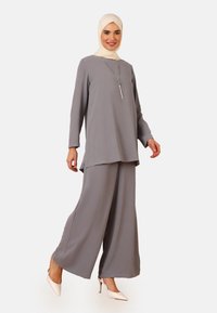 Gray outfit consisting of a long-sleeve top and wide-leg pants, made from textured fabric. Paired with a cream hijab and neutral heels.