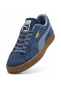 Baskets Puma en daim bleu avec bande bleu clair, lacets à motif, semelle gomme et logo Puma vert sur la languette.