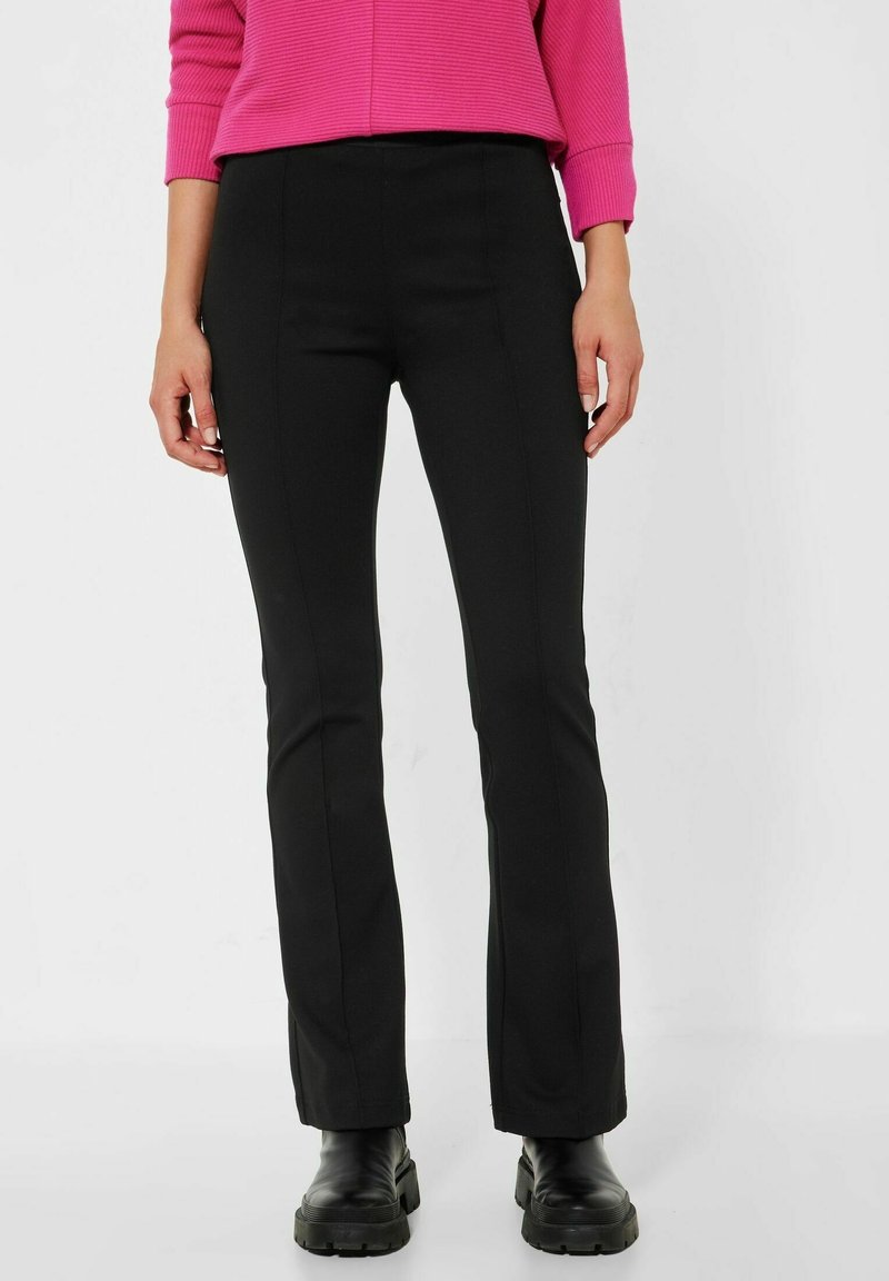 Svarta utsvängda byxor med en slät textur och skräddarsydd passform, med en midjehögt midjeband och rena sömmar, kombinerade med kraftiga svarta stövlar.