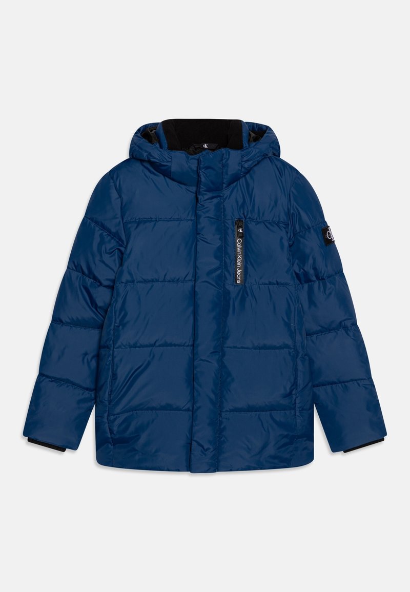 Veste d'hiver matelassée bleu marine avec capuche, poche zippée avant étiquetée "Calvin Klein Jeans" et patch logo sur la manche gauche.