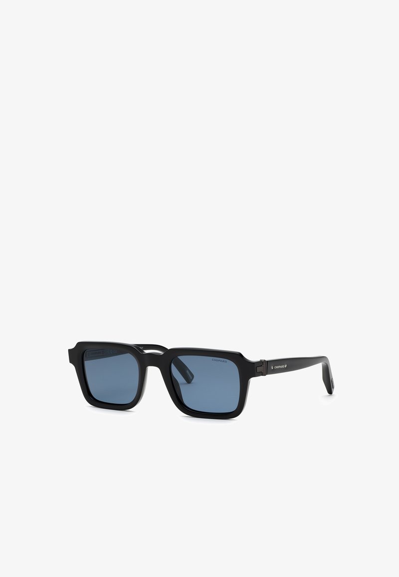 Lunettes de soleil noires à monture carrée avec des verres bleu foncé et des branches fines, légèrement inclinées vers la droite.