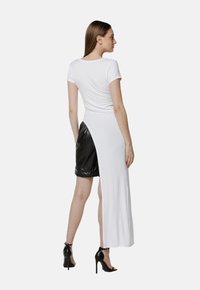 Biała sukienka t-shirtowa z krótkimi rękawami, rozcięciem z tyłu i czarnymi szortami z faux skórki. Gładka tekstura materiału z codziennym krojem.