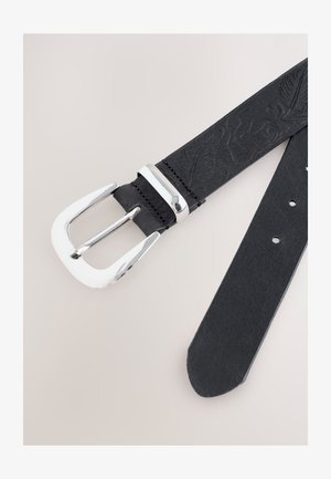 Juodos odos diržas su iškiliais lapų raštais ir blizgančia sidabrine stačiakampio formos sagtimi neutralaus fono.