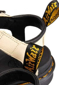 Sandales en cuir noir et crème avec une semelle durable. Présente le logo jaune "AirWair" sur la sangle du talon et des coutures contrastées.
