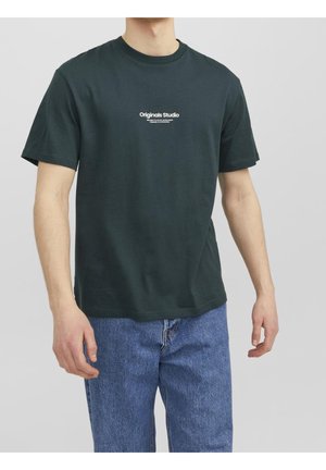 T-shirt en coton vert foncé avec col rond, manches courtes et logo blanc imprimé sur la poitrine. Porté avec un jean en denim bleu.