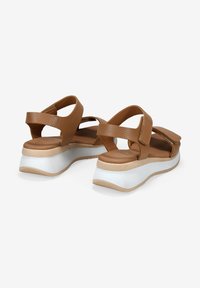 Sandalias de cuero marrón con correas ajustables, suelas de plataforma y bases de goma blanca. Material texturizado con un acabado interior suave.