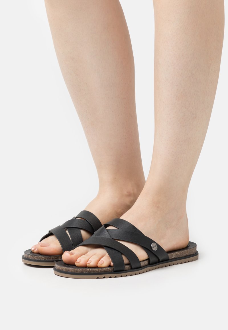 Black leather slide sandals with crisscross straps, rubber sole, and a cork footbed. Features round metal hardware accent.