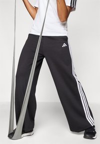Pantaloni de trening negri, cu croi larg, cu dungi albe pe laterale și un logo brodat. Asortați cu un tricou alb și pantofi sport negri.