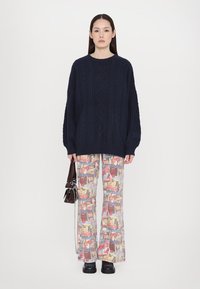 Pull en maille oversize bleu marine avec motif en relief ; pantalon évasé imprimé avec des motifs graphiques variés ; chaussures à plateforme noires ; petit sac à main.