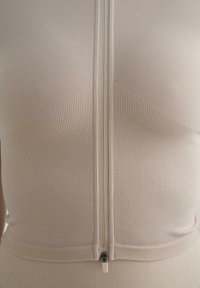 Light beige zip-up top made from ribbed fabric. Features flat seams and a fitted design with a smooth zipper at the center.