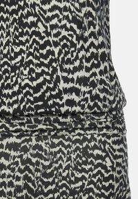 Svart och vit mönstrad tyg med en texturerad, vågig design. Materialet verkar mjukt och något elastiskt, med rynkdetaljer vid midjan.