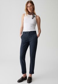 Hose im marineblauen Karo-Muster mit geradem Schnitt, seitlichen Taschen und aufgeschlagenen Säumen, kombiniert mit einem weißen Tanktop und schwarzen Loafers.