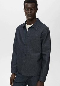 Camicia in denim scuro con design a colletto, chiusura frontale a bottoni e tasca sul petto. Presenta maniche lunghe e una superficie in tessuto testurizzato.