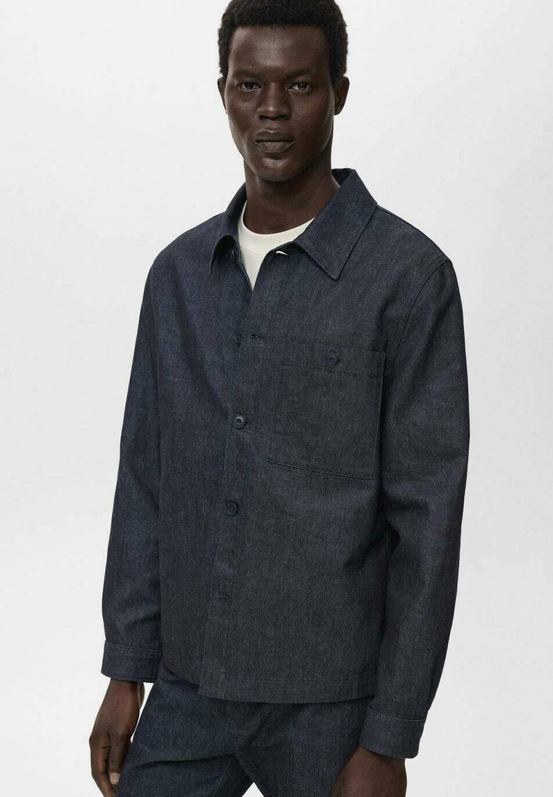 Camicia in denim scuro con design a colletto, chiusura frontale a bottoni e tasca sul petto. Presenta maniche lunghe e una superficie in tessuto testurizzato.