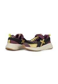 Scarpe sportive nere e oro con accenti viola, dettagli in stampa leopardata e una suola bianca spessa. Le caratteristiche includono lacci e una linguetta sul tallone.