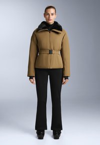 Brown insulated jacket with a black faux fur collar, belted at the waist. Worn over black fitted pants and glossy black shoes.