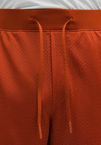 Orange Sportshorts aus atmungsaktivem Mesh-Stoff. Mit einem elastischen Bund mit Kordelzug und kleinen Perforationen für Belüftung.