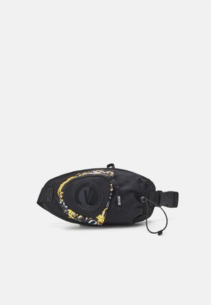 Marsupio nero con toppa rotonda con logo Versace, tasca con zip a motivo dorato, tracolla regolabile e dettaglio con coulisse su sfondo bianco semplice.