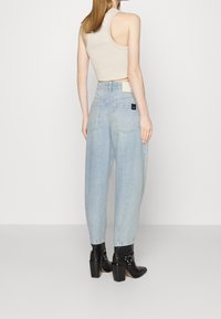 Vaaleansiniset väljät farkut, joissa on korkea vyötärö ja takataskut. Yhdistetty mustiin korkokenkiin ja beigeen ribattuun toppiin.