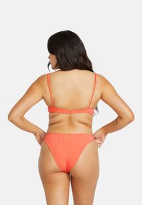 Koraal ribbel bikini met verstelbare bandjes, een sluiting op de rug en minimale bedekking. Gestructureerde stof en subtiele merkdetails.