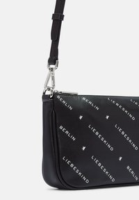 Borsa a polso in pelle nera con tracolla staccabile, caratterizzata da testo bianco diagonale "Liebeskind Berlin" e piccoli loghi di orsetti. Chiusura in metallo argentato.