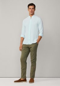 Lichtblauwe blouse met lange mouwen en een mandarin col, gecombineerd met olijfgroene broek en bruine instap schoenen. Glad stof, casual pasvorm.