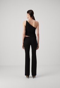 Top nero a spalla unica con texture arricciata abbinato a pantaloni neri aderenti. Entrambi i capi presentano un tessuto liscio e una linea minimalista.