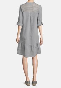 Abito grigio in lino con maniche 3/4, orlo a strati e un dettaglio posteriore a trame testurizzate. Il tessuto ha una finitura morbida e leggermente stropicciata.