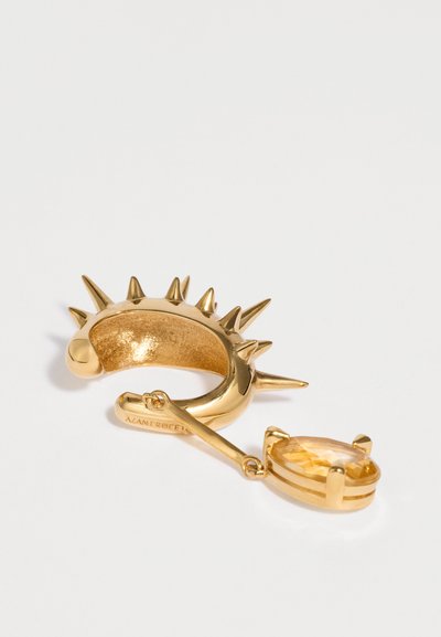 Orecchino a clip dorato a forma di spina con una piccola gemma ambra pendente, incastonata in una montatura ovale con griffe su sfondo bianco.